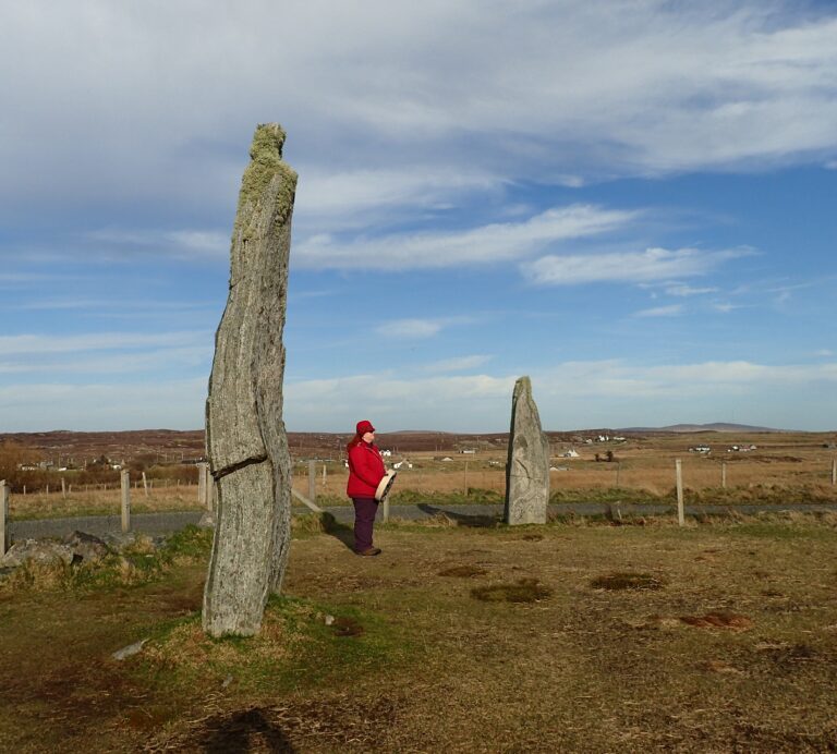A woman in a red coat standing next a tall Calanish stone